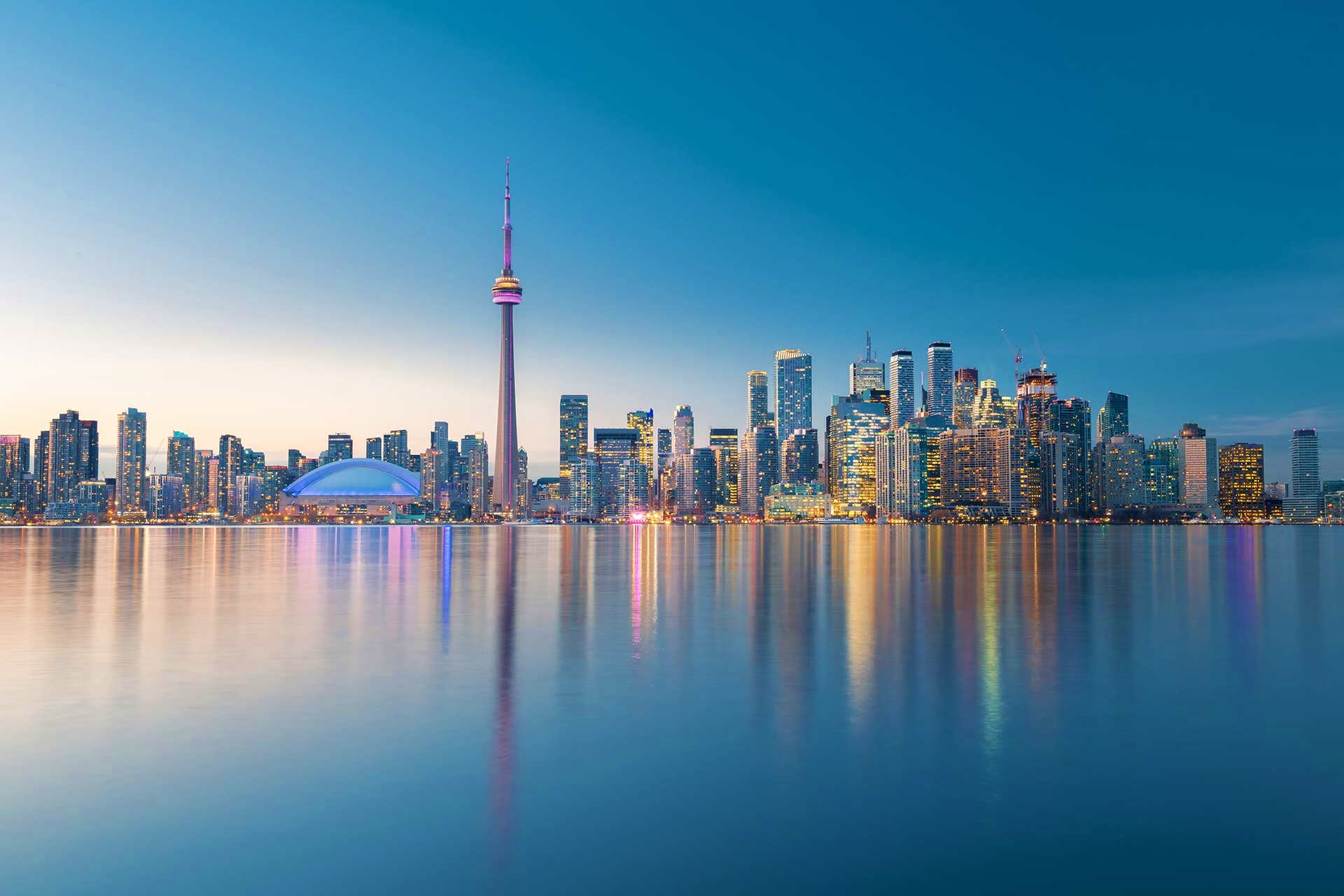 Toronto skyline at dusk with CN Tower and illuminated skyscrapers reflected in calm Lake Ontario waters